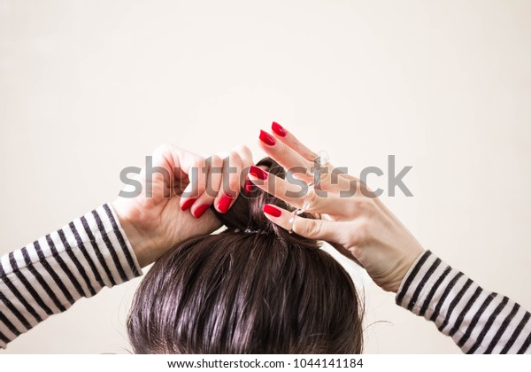 woman is doing her hair, straightened, combing,
the disheveled bun on her head.  Dark hair is tied with a
transparent spiral elastic band. Modern fast hairstyle. Cares about
a beautiful hair.
Copyspac