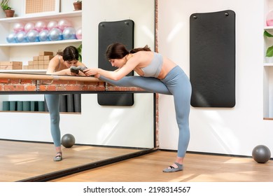 Woman doing leg stretching exercises in a barre in a gymnasium in a health and fitness concept reflected in a wall mirror - Powered by Shutterstock