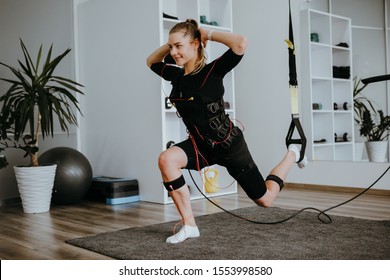Woman doing lunges in EMS electro stimulation suit with cables, using TRX.