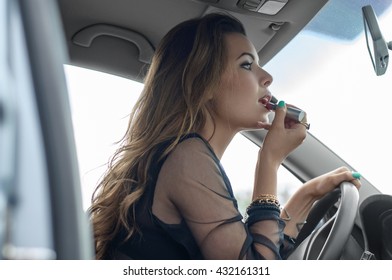 Woman doing make-up while she sits in the car. She applies lipstick and looking in the rearview mirror. Concept: lifestyle, spontaneity, femininity - Powered by Shutterstock