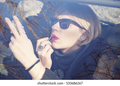 Woman doing make-up while she sits in the car. She applies lipstick and looking in the rearview mirror - Powered by Shutterstock