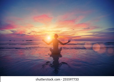 Woman doing meditation near the ocean beach. Yoga silhouette. - Powered by Shutterstock