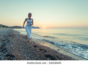 Woman is doing morning excercises at the sea during sunrise