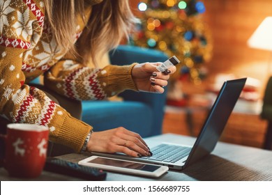 Woman Doing Online Shopping At Christmas: She Is Sitting On The Sofa At Home, Connecting With Her Laptop And Holding A Credit Card, Christmas Tree In The Background