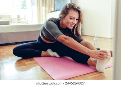 Woman doing online yoga class with laptop in the living room at home in the morning. Fit woman high body flexibility stretching her leg and back to warm up doing aerobics gymnastics exercises at home. - Powered by Shutterstock