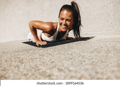 Woman doing push ups on exercise mat. Female in sportswear smiling during her workout.