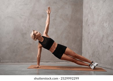 Woman doing the side plank exercise on mat in gym. Pretty girl wearing shorts and short top standing in side plank on one hand at gym, training body core and balance, strengthening abs muscles. - Powered by Shutterstock