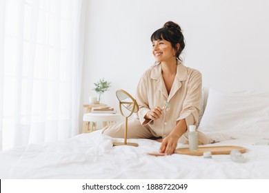 Woman Doing Skin Care Massage Sitting On Bed, Smiling Woman Using A Roller To Massage Face.