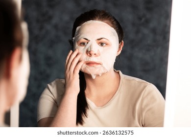 Woman doing skincare ritual with hydrating face mask. Evening beauty routine to soothe facial skin after hard day. Self care concept