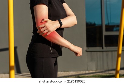 Woman doing sport and suffering from elbow pain. Female holding painful arm with red point during training outdoors. Injury consequences. High quality photo - Shutterstock ID 2196139025