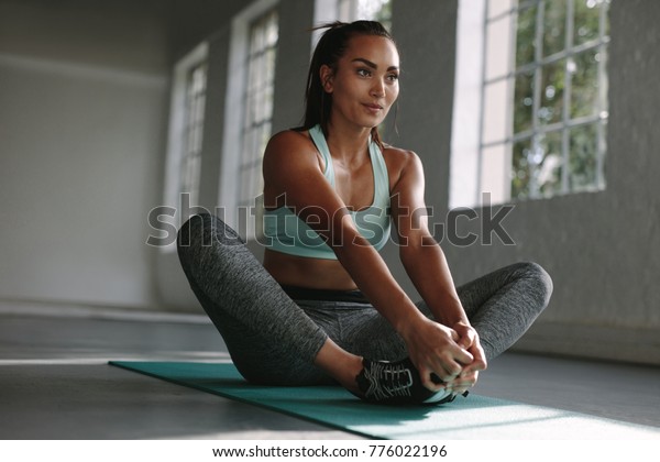 Woman doing stretches on exercise mat in gym.\
Baddha Konasana being performed by fitness female at gym. Cobbler\
pose stretching workout.
