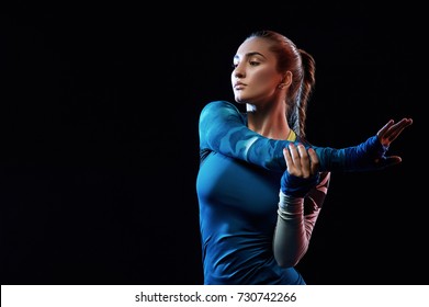 Woman doing stretching exercises. Fit young female boxer in sportswear isolated on black background