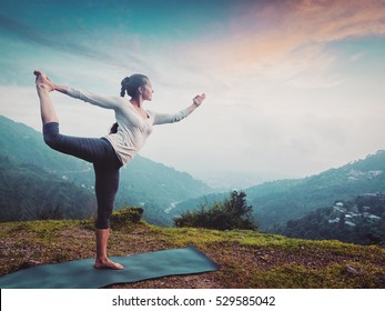 Woman doing yoga asana Natarajasana - Lord of the dance pose outdoors at waterfall in Himalayas. Vintage retro effect filtered hipster style image. - Shutterstock ID 529585042