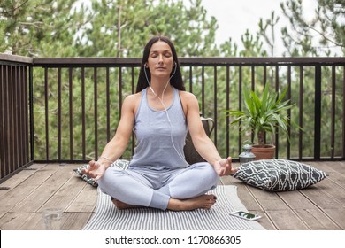 Woman doing yoga with earphones on a balcony in nature - Powered by Shutterstock