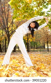 Woman Doing Yoga Exercises In The Autumn Park. Beauty Nature Scene With Colorful Foliage Background, Yellow Trees And Leaves At Fall Season. Autumn Outdoor Lifestyle. Happy Woman On Fall Leaves