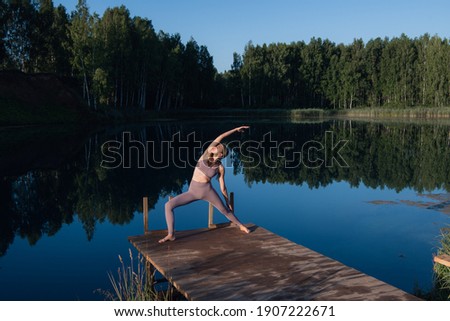 Woman doing yoga on a forest lake. Beautiful girl doing exercises on stretching and flexibility outdoors
