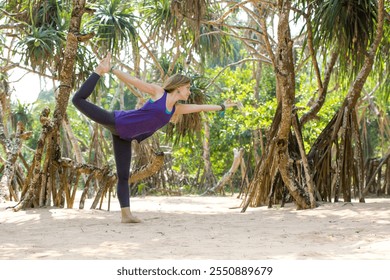 A woman is doing a yoga pose on the beach under the palm trees. She is wearing a purple tank top and black pants - Powered by Shutterstock