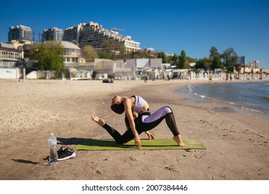 Woman Doing Yoga Stands In A Triangle Position On The Public Beach.