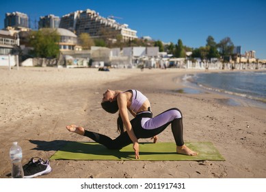 Woman Doing Yoga Stands In A Triangle Position On The Public Beach.