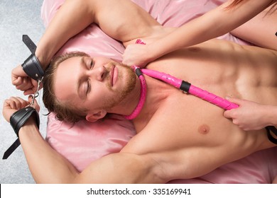 Woman Dominates The Man With Lash, Handcuffs And Pink Whip. Couple In Bed. Sex Toys