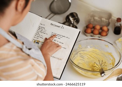 Woman, dough and recipe book for baking in kitchen with ingredients for muffins, hobby and flour. Menu, female person and home for cookies or cake with instructions, steps and culinary for dessert