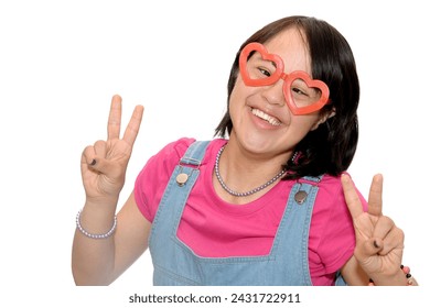 Woman with down syndrome.
Making the victory sign, smiling looking at the camera showing fingers making the v, number two. dressed in casual clothes and heart-shaped glasses. Trisomy 21.
