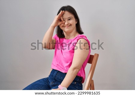 Woman with down syndrome wearing band aid for vaccine injection smiling happy doing ok sign with hand on eye looking through fingers 