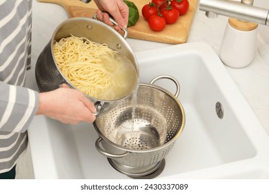 Woman draining pasta into colander at sink, closeup