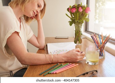 Woman Drawing An Adult Coloring Book While Comfortably Sitting At Table By A Window.