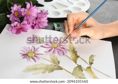 Woman drawing beautiful chrysanthemum flowers in sketchbook at black table, closeup