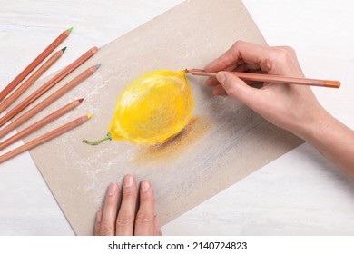 Woman drawing lemon on paper with pastel pencil at white wooden table, top view - Powered by Shutterstock