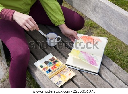 a woman draws a sketch with watercolors in a notebook in the open air and drinks