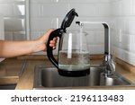 A woman draws water into an electric kettle in the background of the kitchen. It