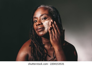 Woman With Dreadlocks Applying Moisturizing Cream On Her Face. Confident Dark-skinned Woman Taking Care Of Her Flawless Melanated Skin. Mature Black Woman Ageing Gracefully.