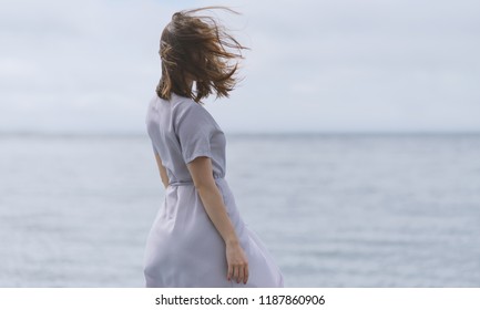 Woman in dress enjoys a walking near the sea shore. View from back.