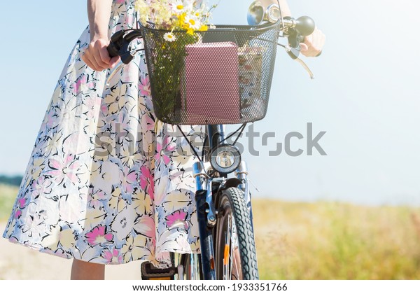 Woman in dress with flowers\
carries wild flowers bouquet on bicycle in basket , flowers \
gathered in a meadow  by woman in the countryside in summer time\
sunny day
