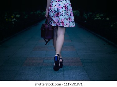 Woman In A Dress In Heels Walking Through The City Street Park Flowers Night Nature Blur Background