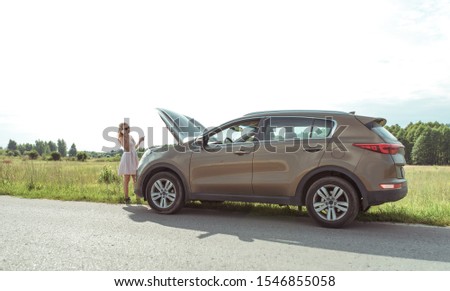 woman in dress on road, makes phone calls, crossover car, an open hood, problem on road, broken car, tow truck call, ambulance, police and emergency services. In summer, outside city on highway