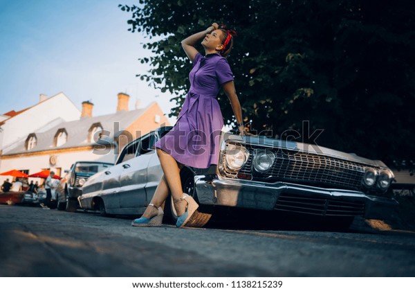 Woman\
in dress is sitting on the fender of old muscle\
car