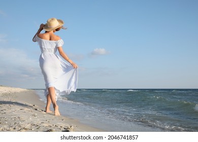 Woman in dress with straw hat walking by sea on sunny day, back view