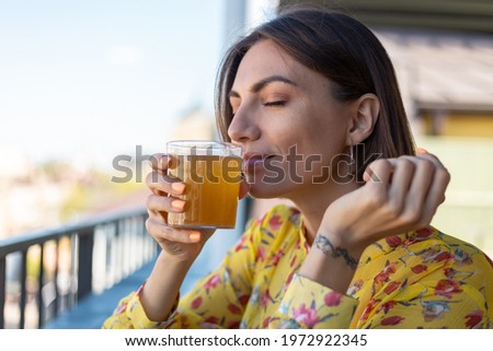 Woman in dress in summer cafe enjoying cool kombucha  glass of beer sniffing smell with eyes  closed