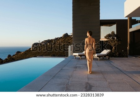 Woman in dress walking along infinity pool overlooking ocean