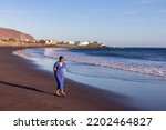 Woman in dress walking on the beach Playa Valle Gran Rey during sunset seen from Promenade de Playa de La Calera in Valle Gran Rey on La Gomera, Canary Islands, Spain, Europe. Dark volcanic sand beach