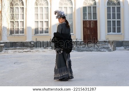 a woman dressed as a 19th century noblewoman stands near an old manor house.russian winter.