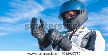 woman dressed as a biker with black safety helmet putting on her leather gloves getting ready to ride a motorcycle