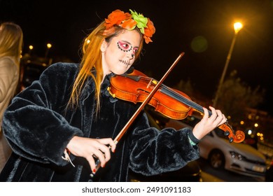 A woman dressed in black and wearing a flower headband is playing a violin. The scene takes place at night, with a car parked in the background. At the Halloween party at night in the city - Powered by Shutterstock