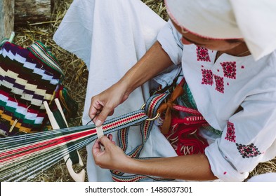 Woman Dressed In Colorful Traditional Native Serbian Closing Knitting A Carpet With National Pattern