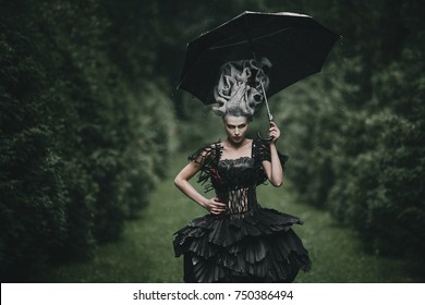 Woman dressed like a hero from 'Alice in Wonderland' poses with black umbrella in a green park