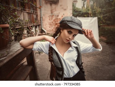  woman is dressed like a man, retro hooligan in cap. The Peaky Blinders. Clothes shirt black pants, gray vest, pretty face. young girl sexy model cat's eyes look close up. fashion men clothing 20s 30s