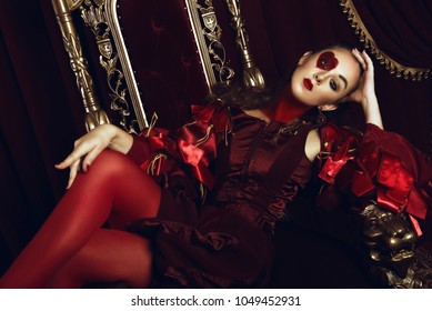 Woman dressed as the queen of hearts, creative make up with big heart on eye, girl sitting in the throne, hi-end retouched portrait. Conceptual photo - Shutterstock ID 1049452931